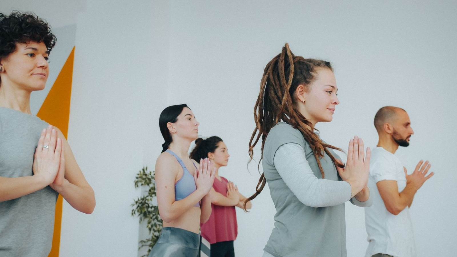 In a bright studio, four adults dressed for exercise press their palms together in a prayer pose.