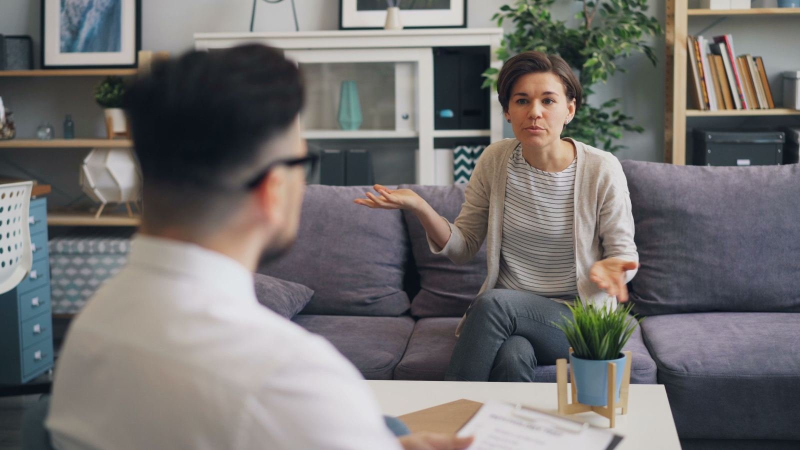 A woman uses hand signals while speaking with a man in a well-lit room.
