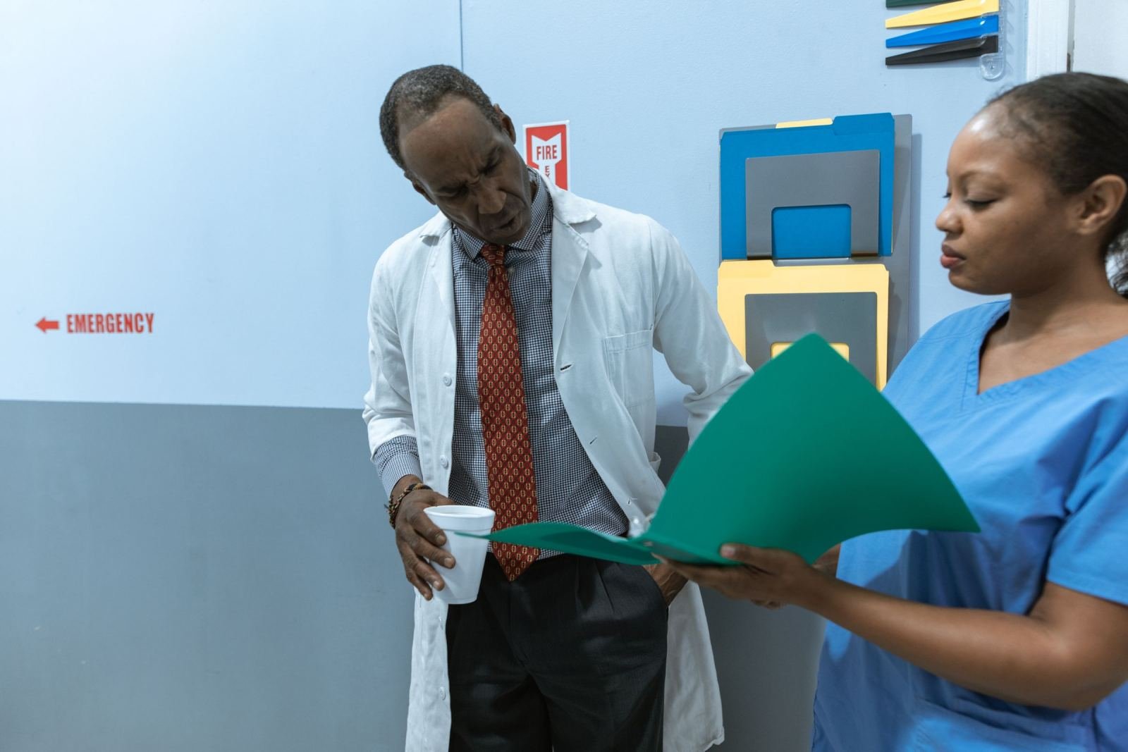 A doctor in a white coat and a nurse in blue scrubs review a green folder