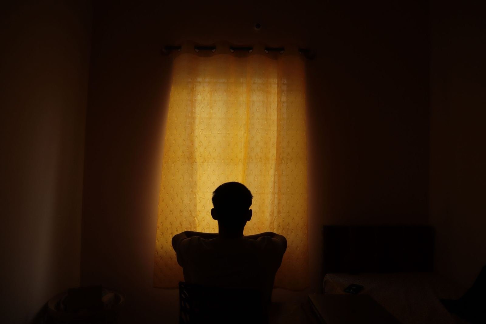 A person sits by a window with yellow curtains.