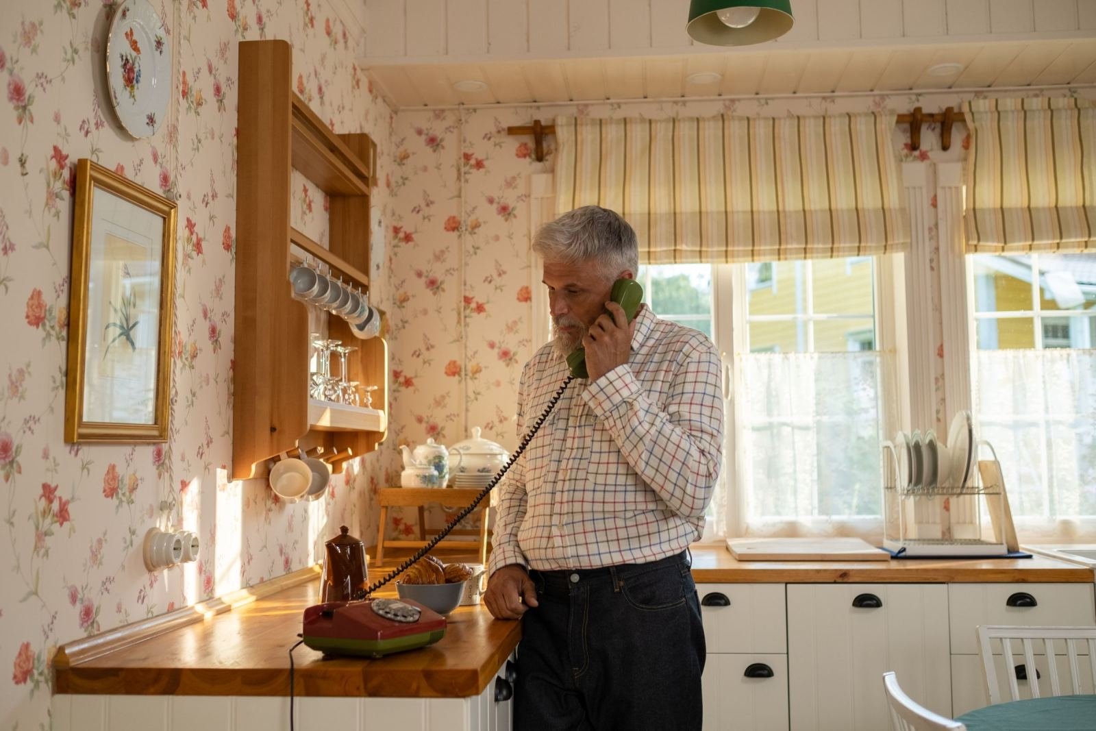 A man in a plaid shirt talks on a green corded phone in a kitchen
