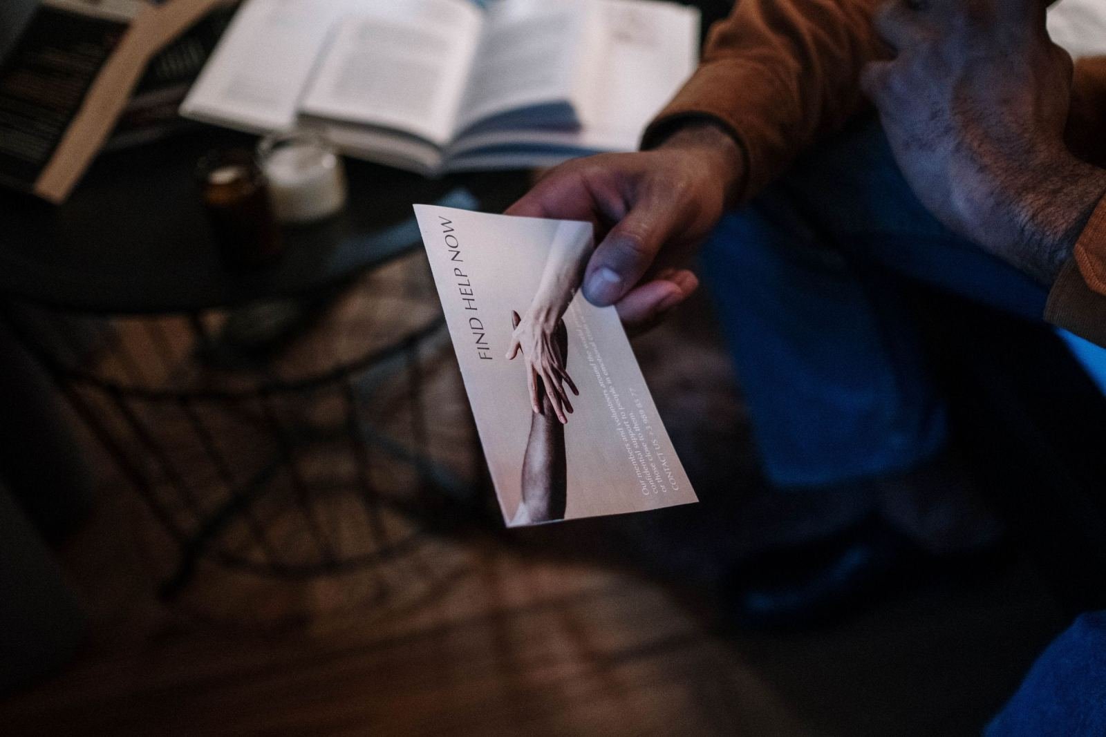A person holds a brochure that says 'FIND HELP NOW' with a photo of two people holding hands