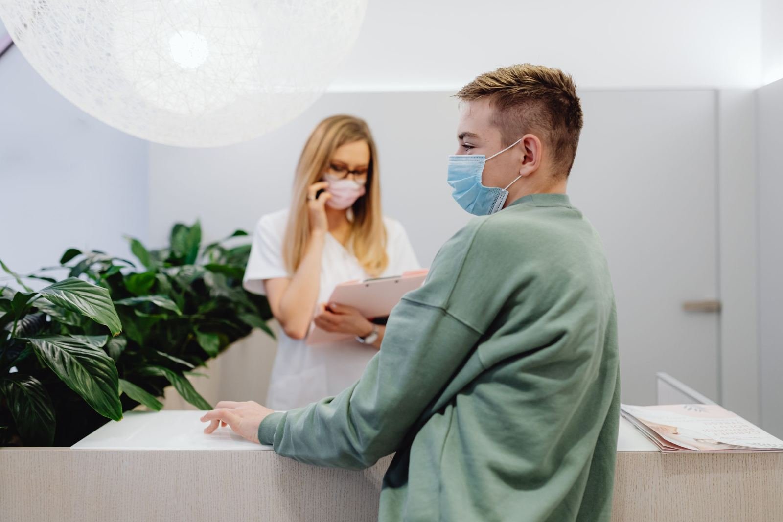 A masked man speaks with a medical professional at a clinic front desk