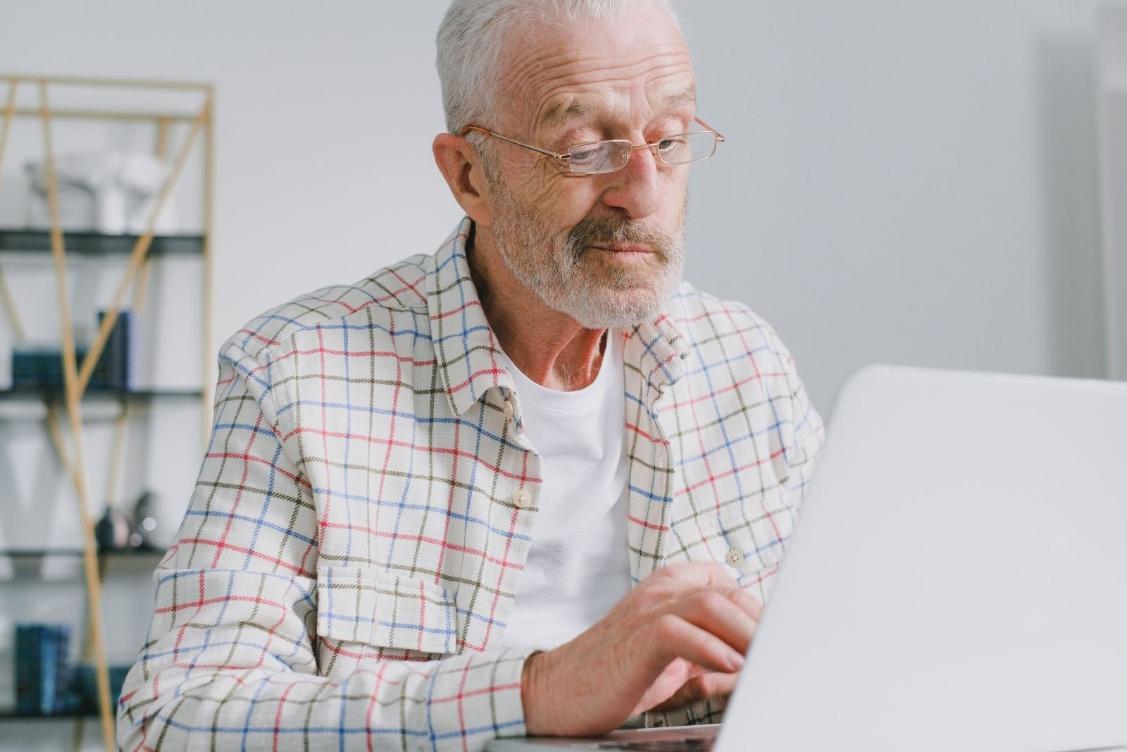 A man with older features and glasses types on a laptop at his desk
