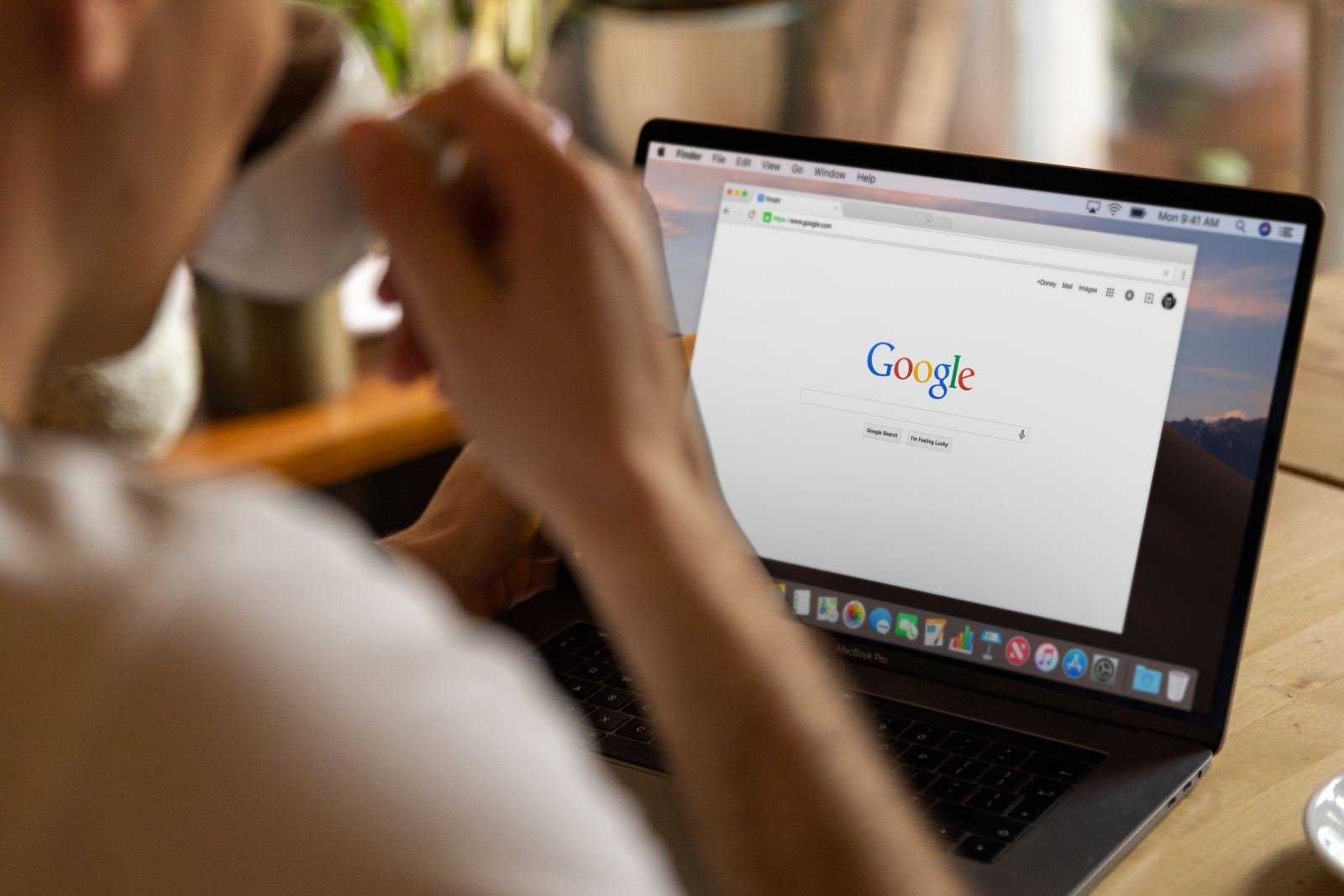 A person holds a mug and looks at a Google search page on a laptop.