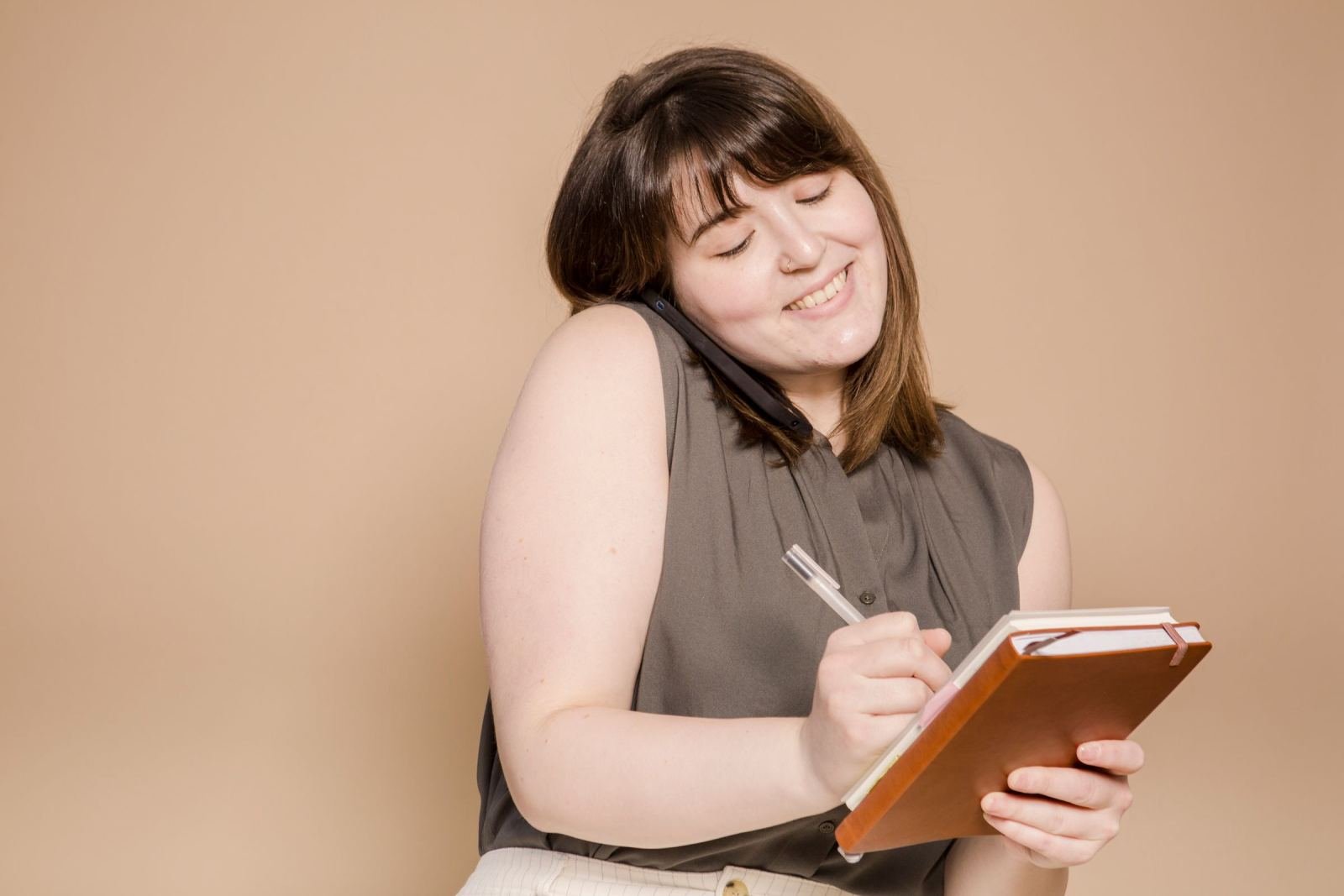 A lady chats on a phone and writes in a book.