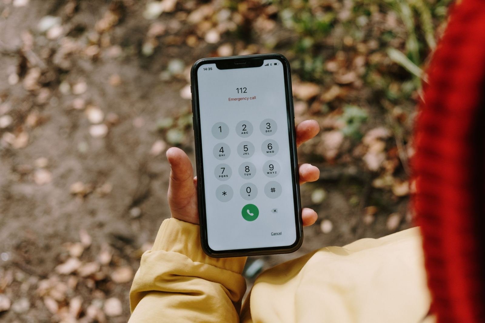 A person in a yellow jacket holds a phone dialing an emergency number