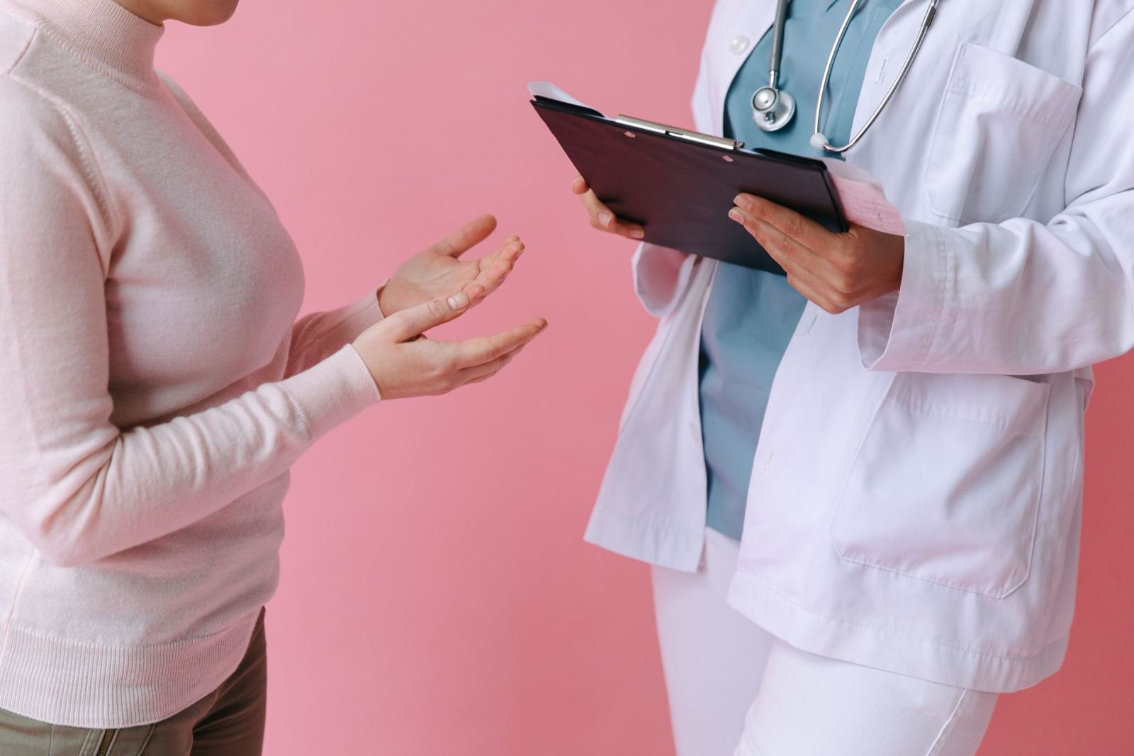 A person in a white sweater talks to a clinician who holds a clipboard