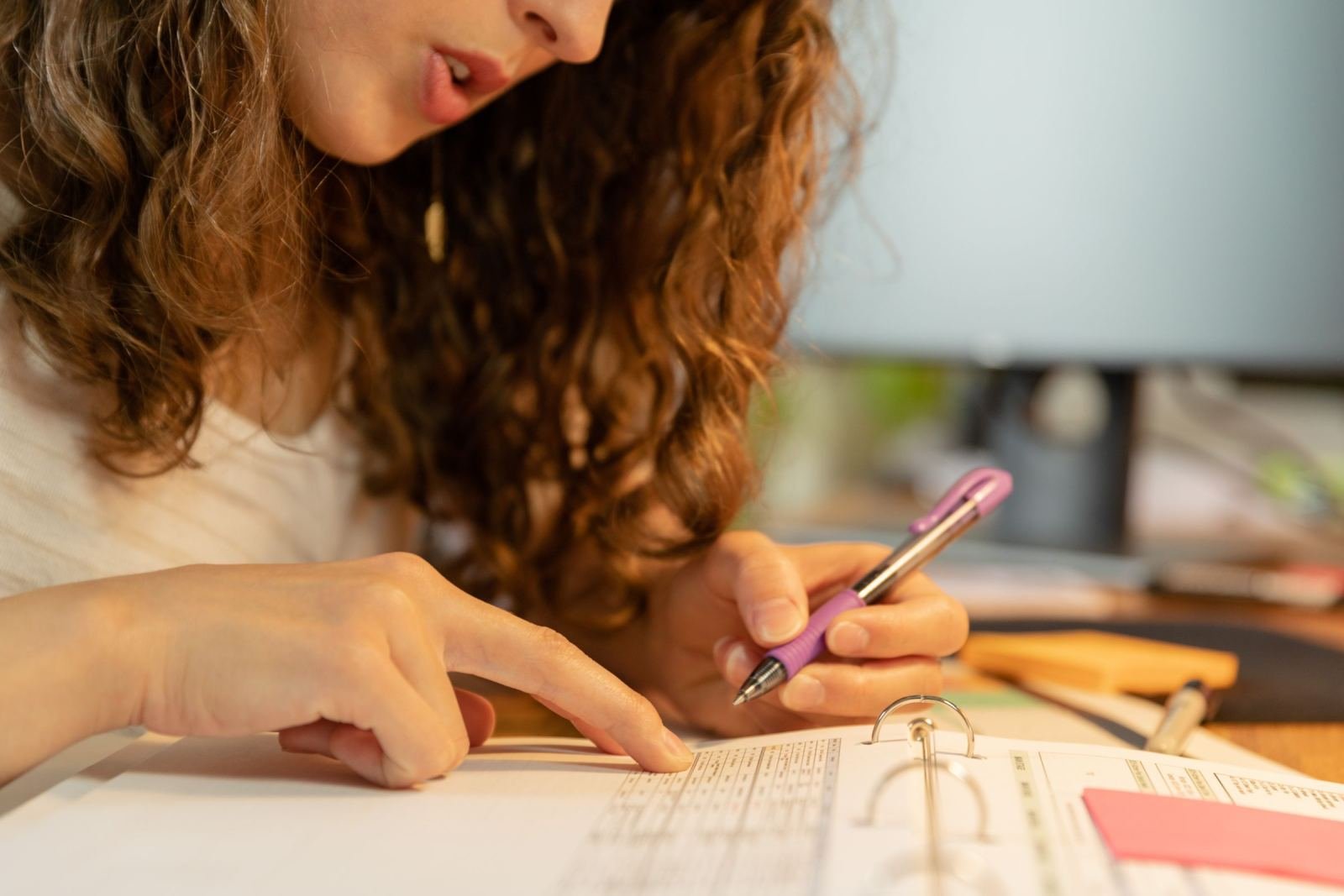 A person with curly hair uses a purple pen to point at a ring-bound planner