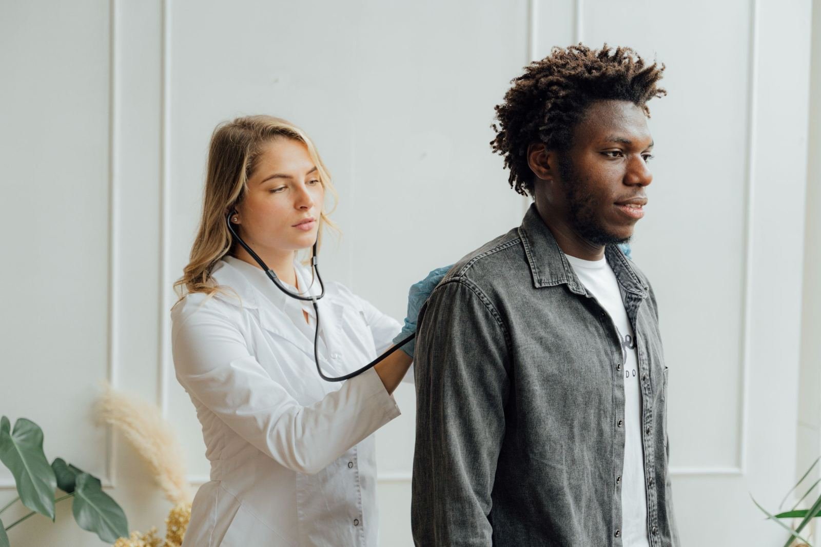 A doctor wearing a white coat checks a man's back with a stethoscope