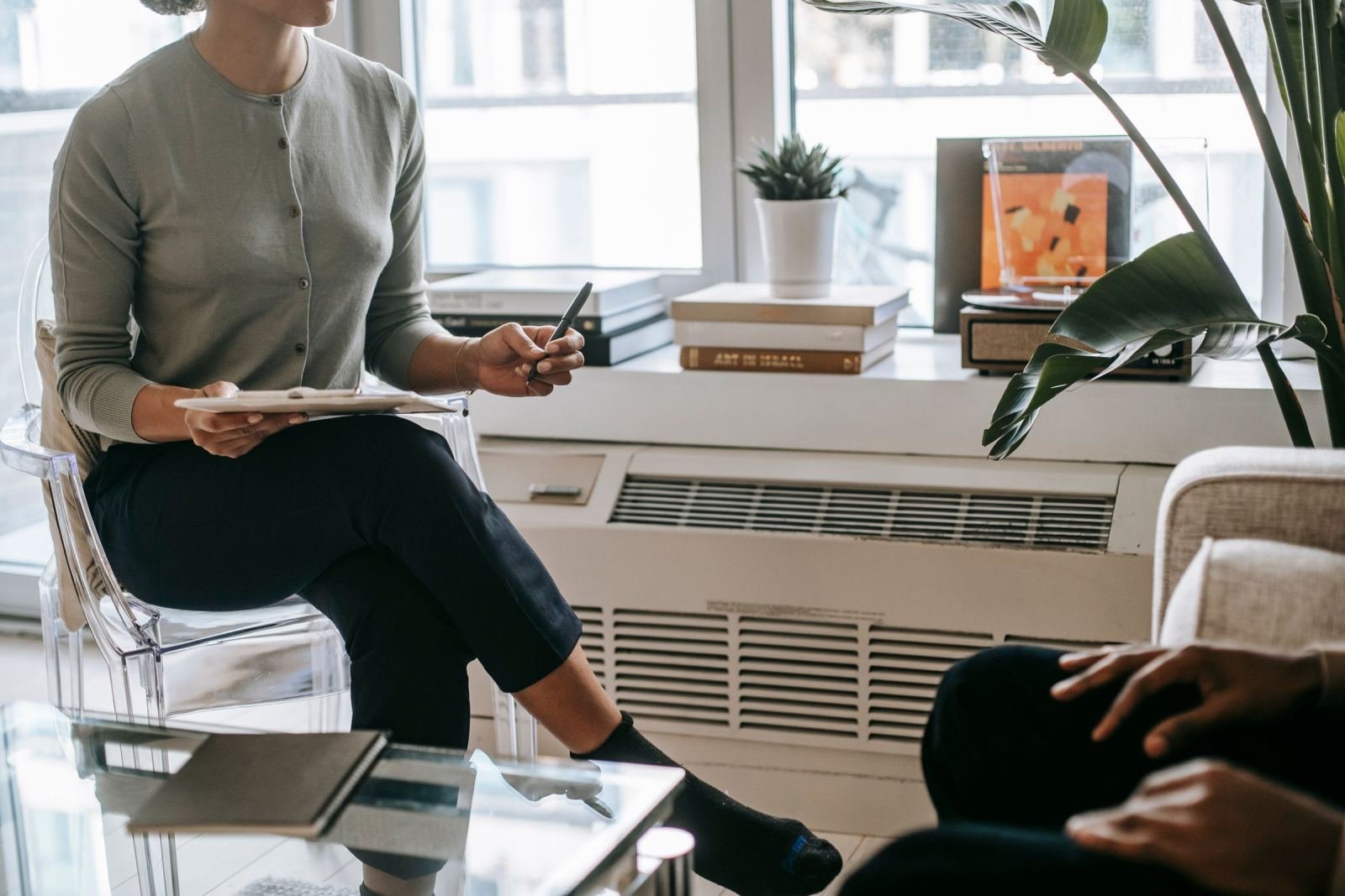 A clinician with a clipboard sits in a bright room talking to a client