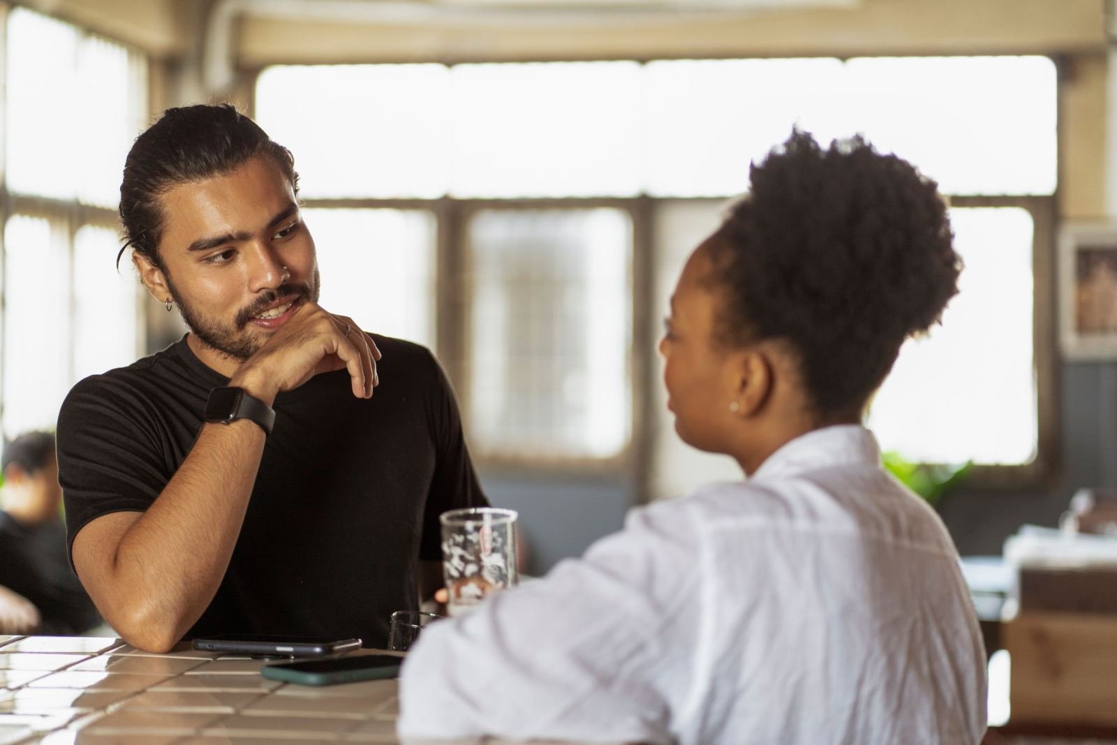 A man and woman sit at a counter and talk in a bright room