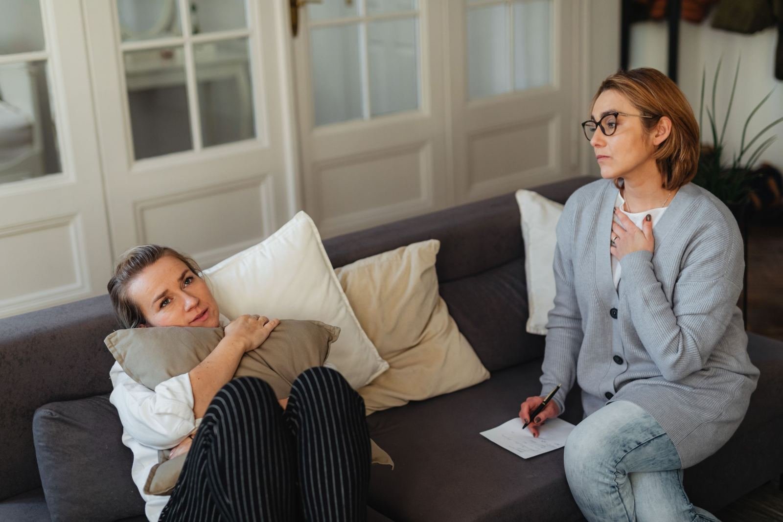 A counselor takes notes while a woman lies on a couch and talks.