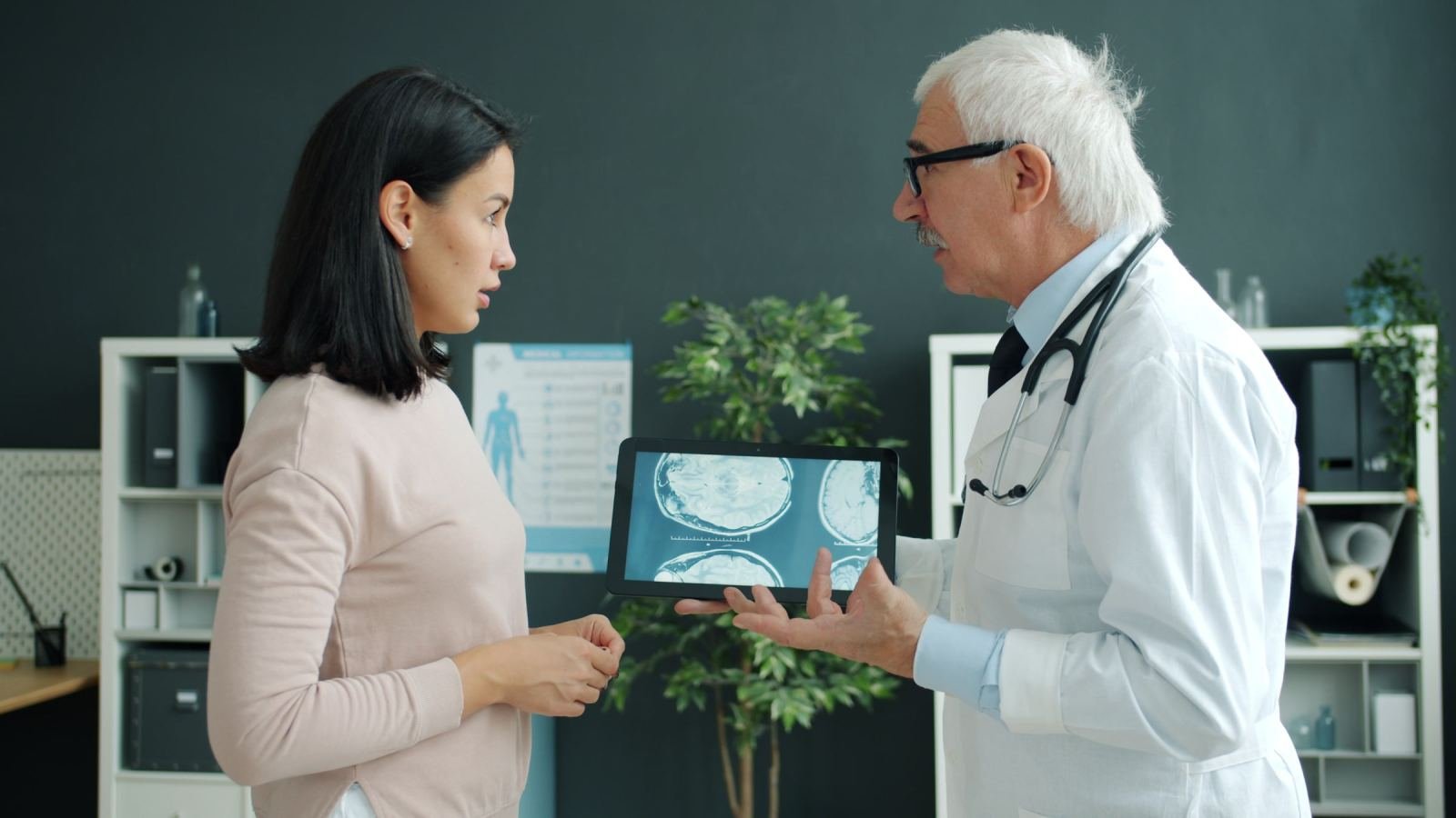 A woman views brain scans on a tablet with a doctor in a white coat.