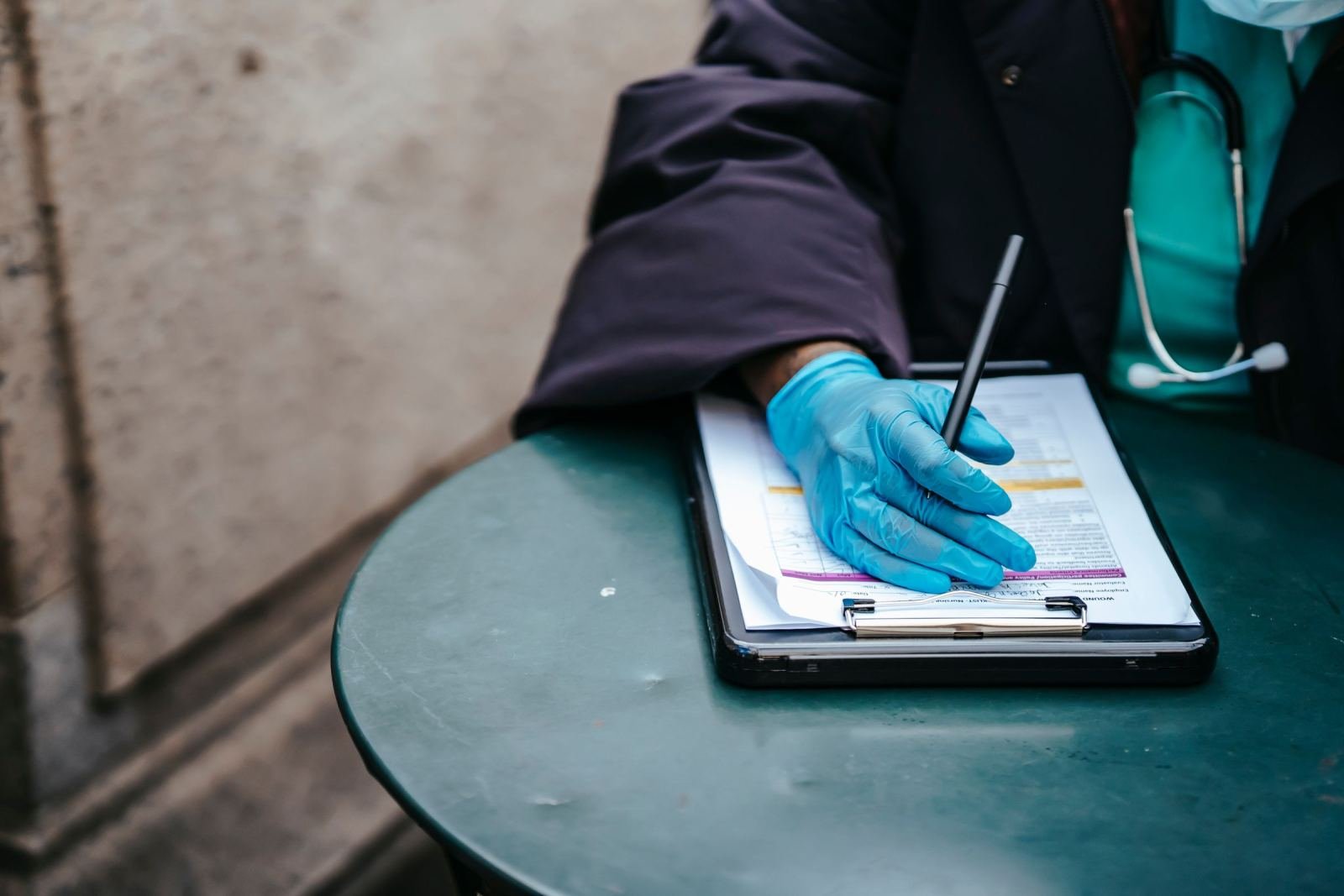 A healthcare provider in a blue glove writes on a clipboard at a green table