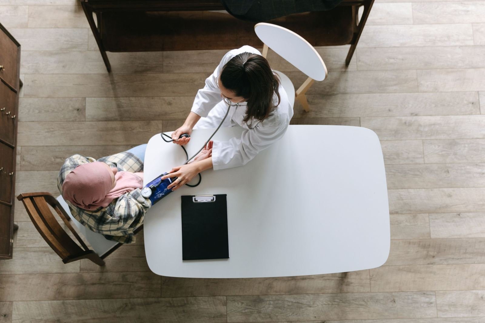 A clinician in a white coat takes a patient's blood pressure at a white table