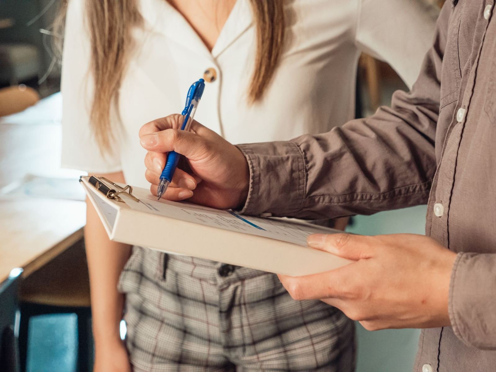 One person stands beside another who is writing on a clipboard.