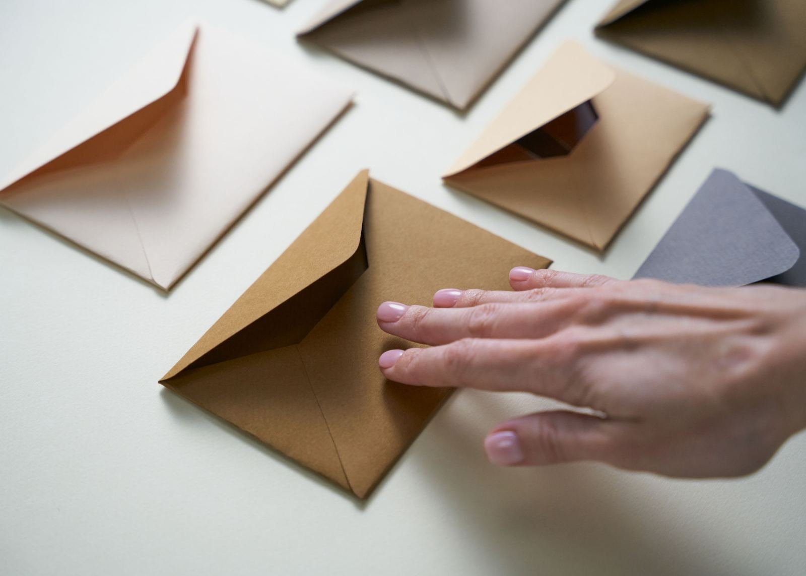 A hand resting on an open brown envelope among other open envelopes on a white surface