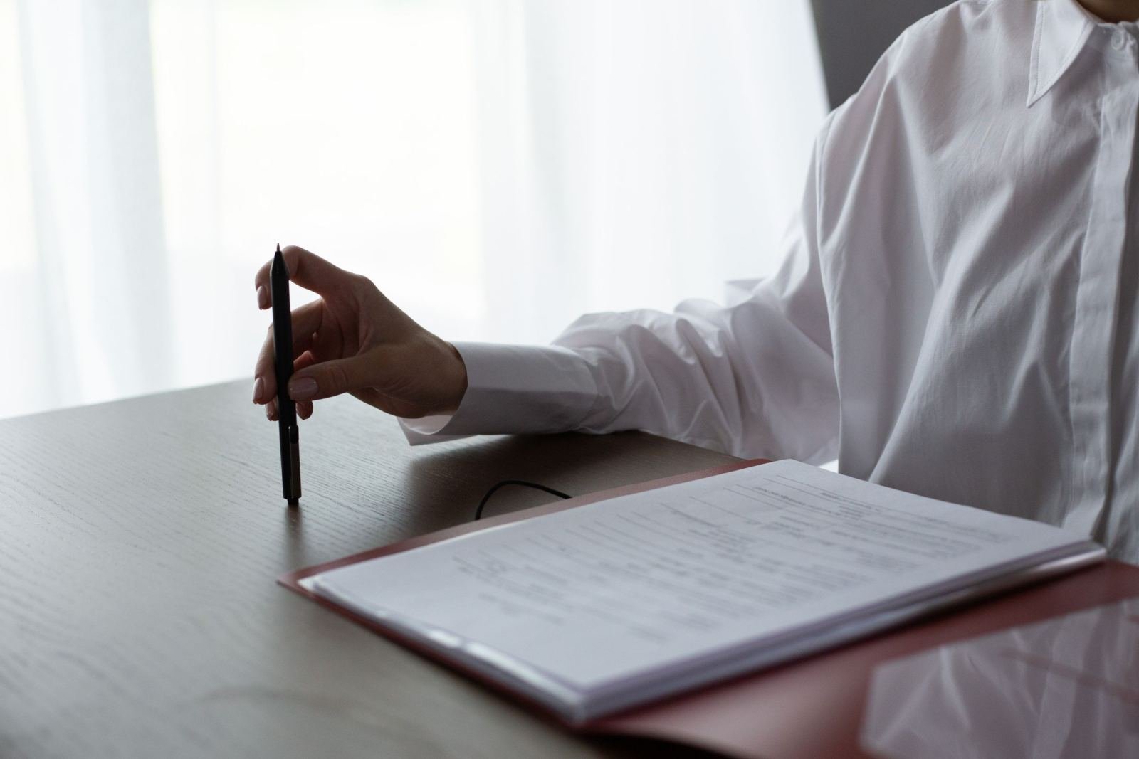 A person in a white shirt holds a pen over documents in a red folder