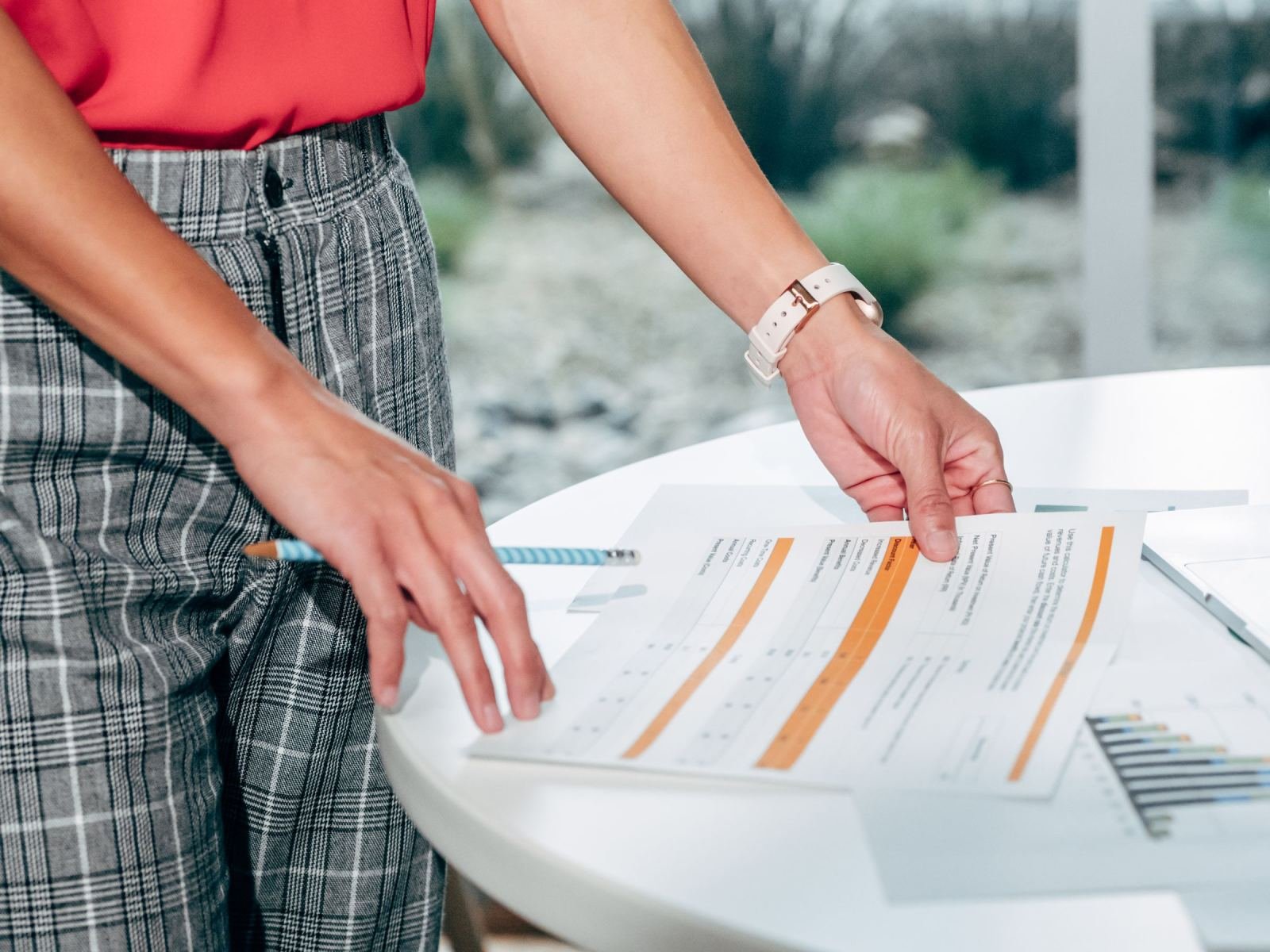 Someone in plaid pants looks over a marked-up paper on a white surface