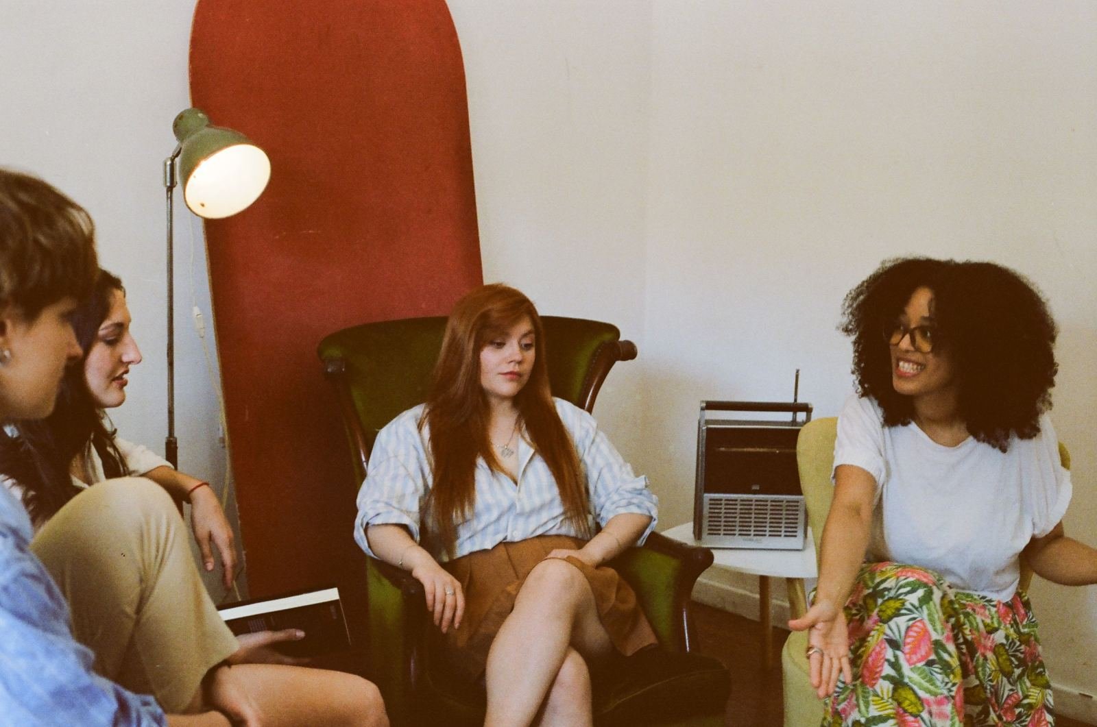 A bright room holds three women. They sit in a circle and chat.