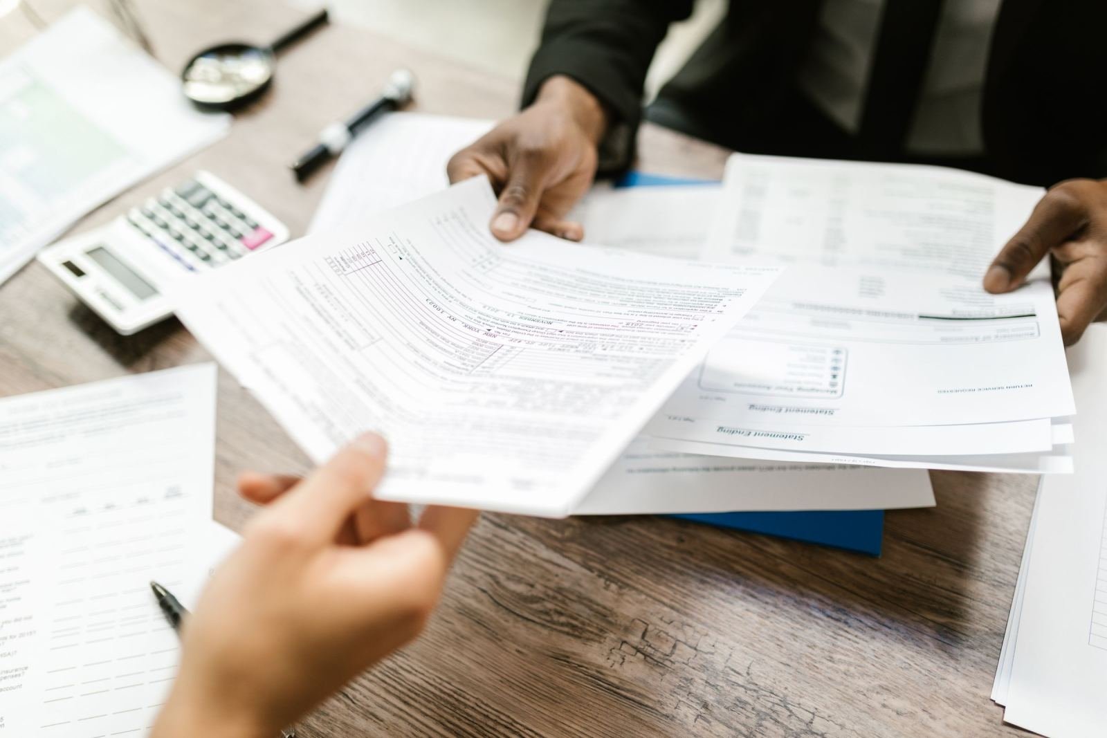 Two people review printed documents and paperwork at a wooden desk