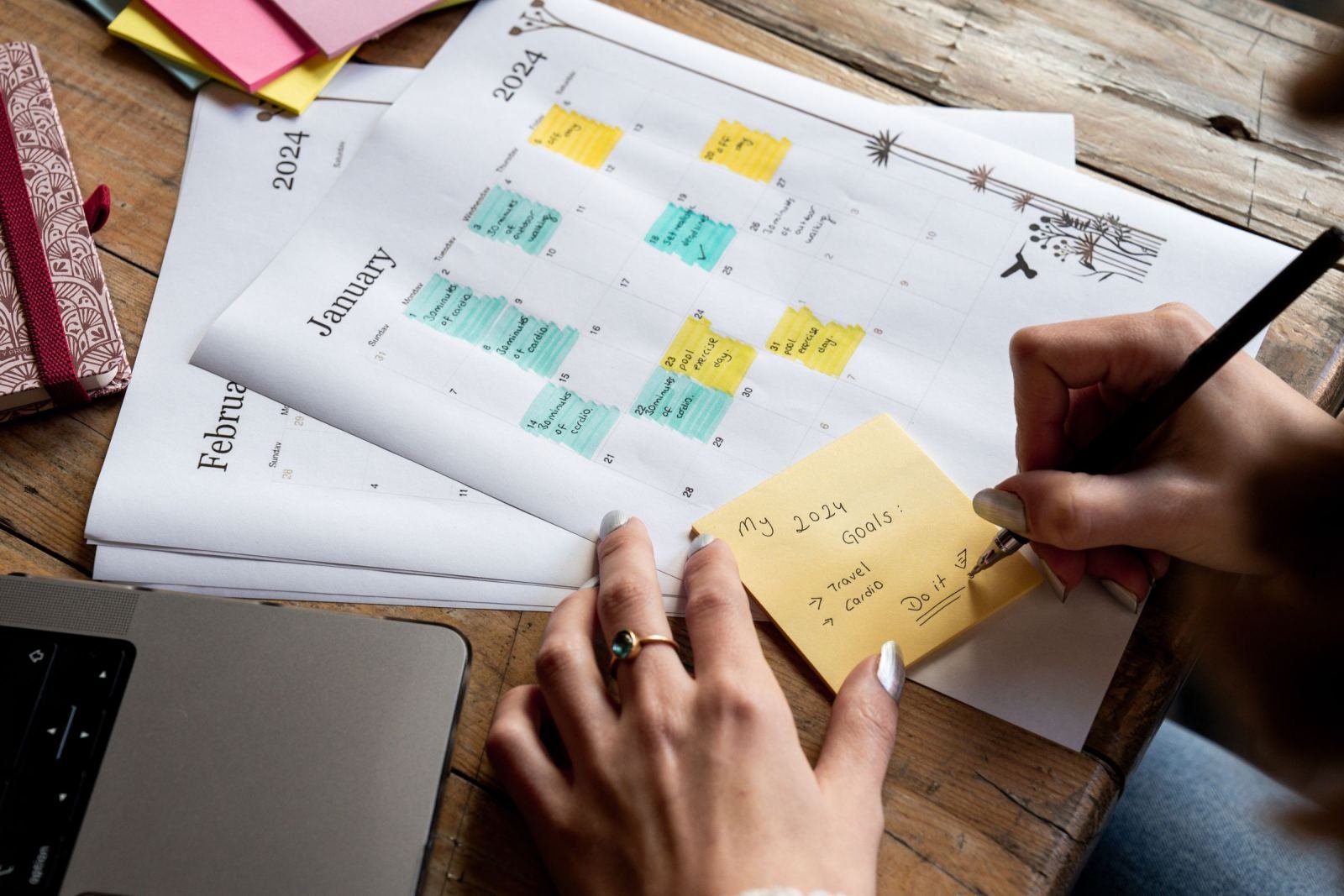 A person writes goals on a sticky note placed on a 2024 calendar.