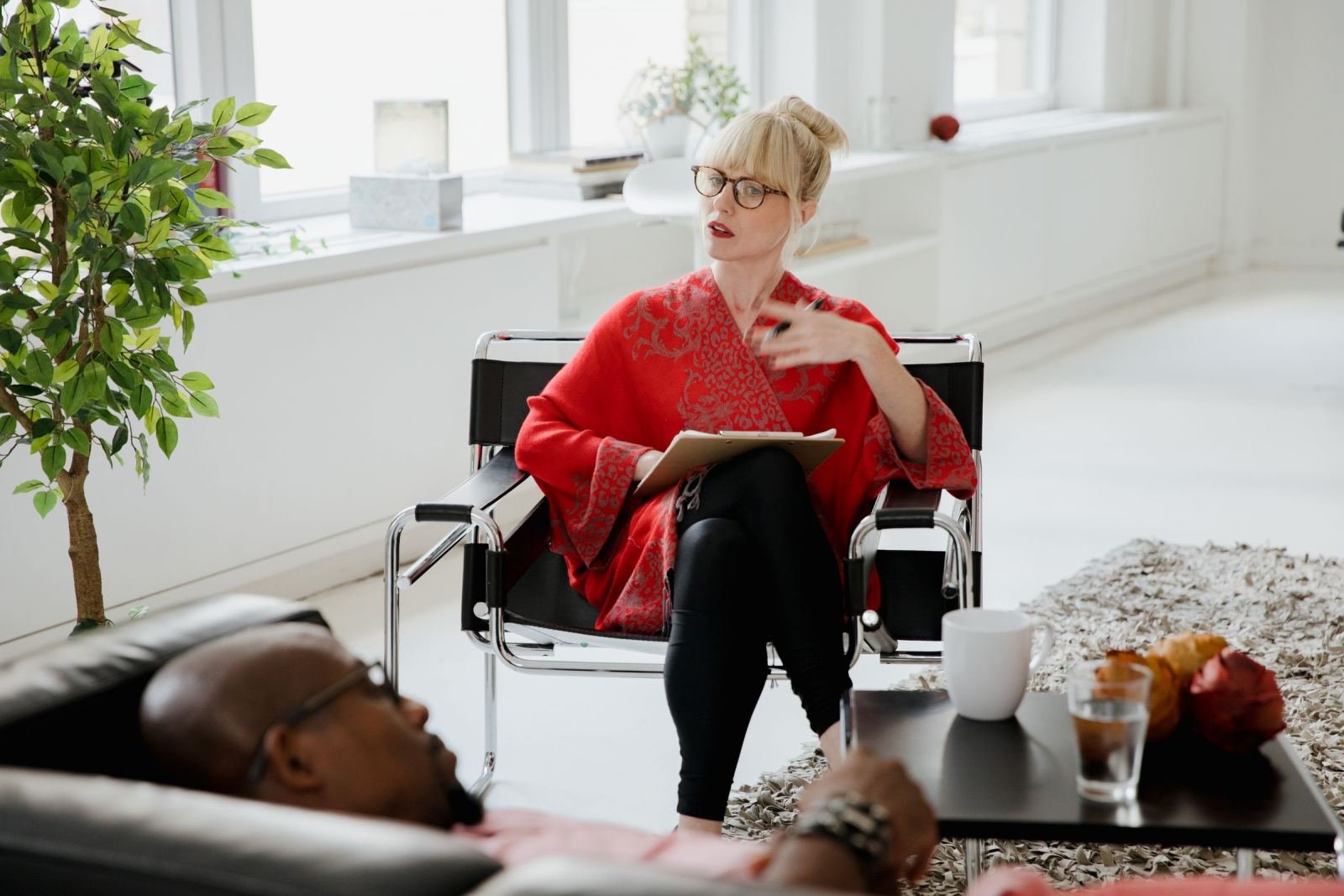 A doctor holds a pad while talking to a man lying on a couch.