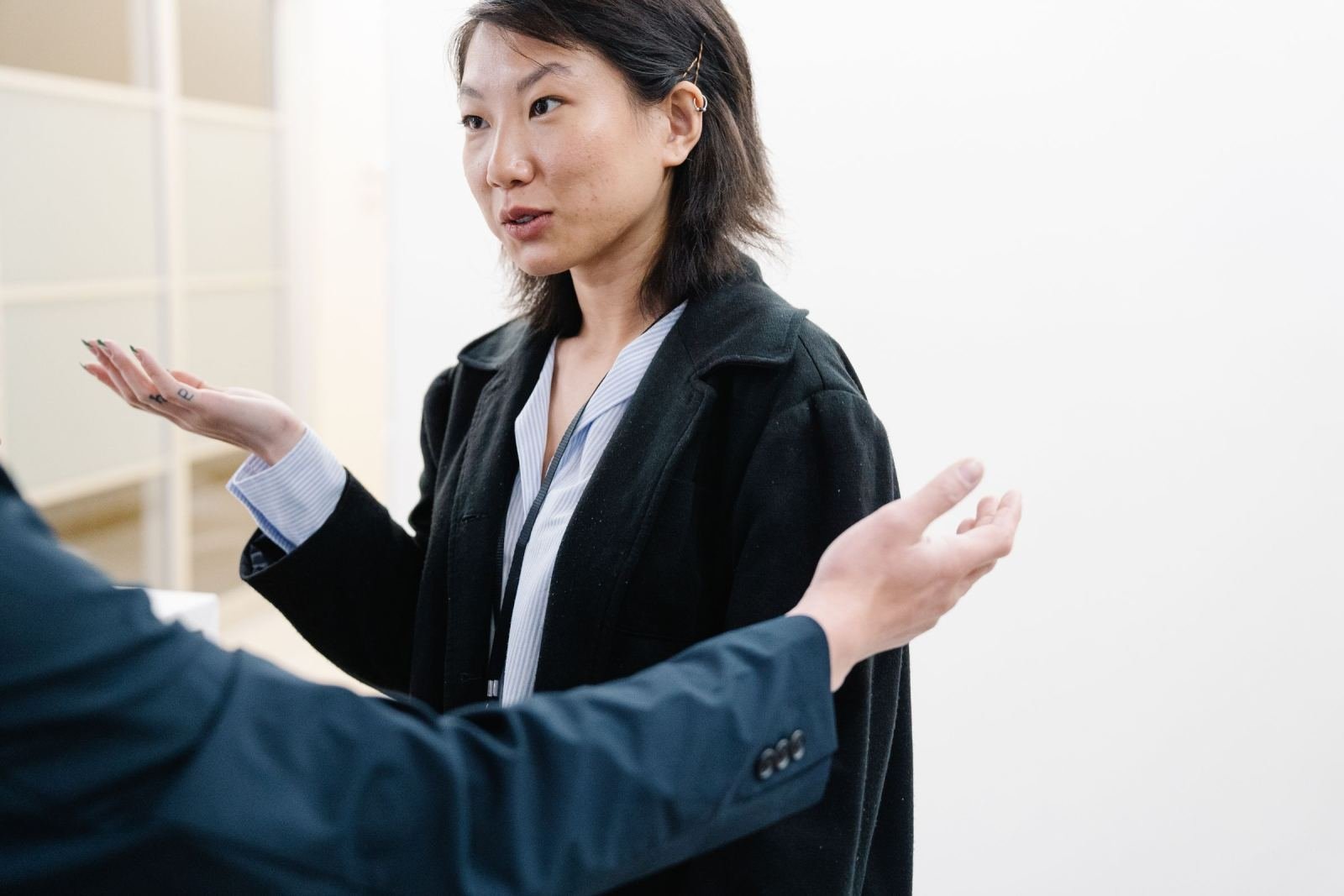 A woman wearing a black coat uses her hands to talk to someone else.