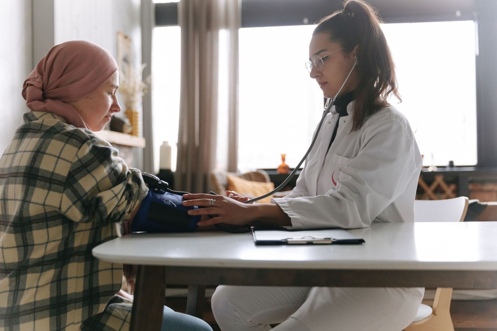 A doctor in a white coat measures the blood pressure of a woman in a hijab